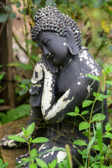 A weathered, black stone Buddha in a garden - vertical