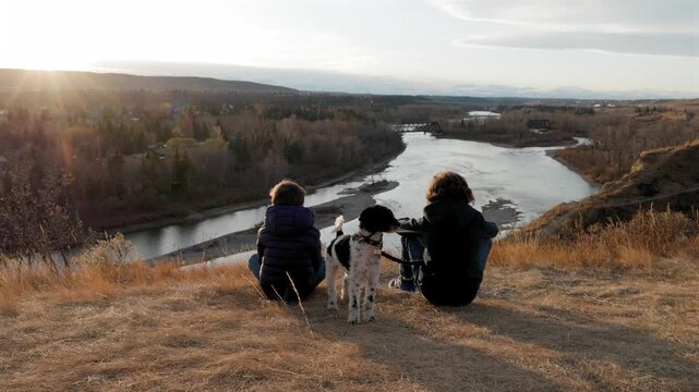 Two young boys sitting with their dog on top of a hill at Bowmont Park watching the sunset