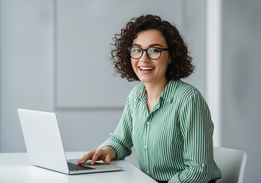 Cheerful young woman with glasses working on a laptop at her desk.