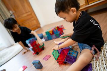 Close-up of a young boy concentrating on magnetic tiles while his brother plays in the background,...