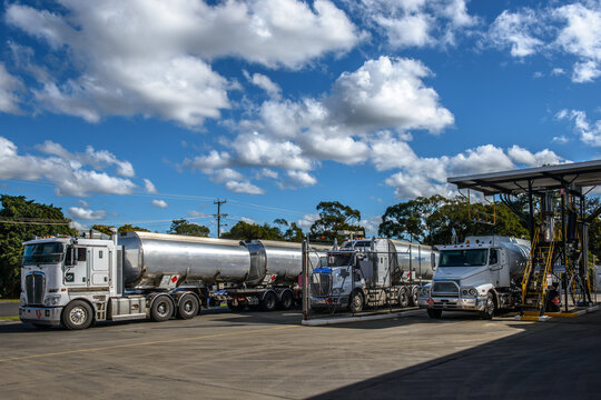 Petrol tankers refilling at a depot under fluffy clouds in a blue sky- horizontal