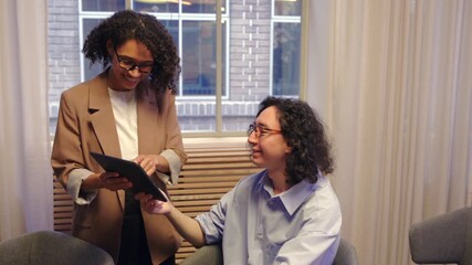 Two colleagues discussing business ideas in a bright modern office using a digital tablet and laptop showing communication cooperation and creative teamwork in professional workplace - Powered by Adobe