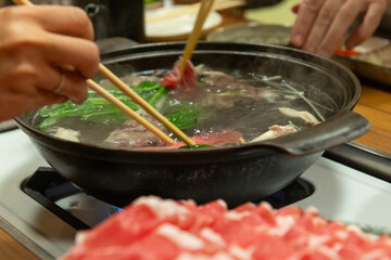 しゃぶしゃぶを囲む食卓の調理シーン　ラム肉と野菜を鍋で茹でる様子