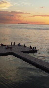 Verticel. People sitting on pier, low drone shot over Koh Phangan coastline, sunset time