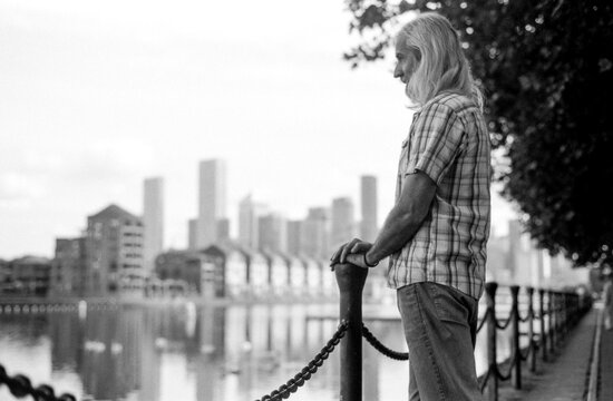Senior man contemplating city skyline by the river in monochrome film style - Powered by Adobe