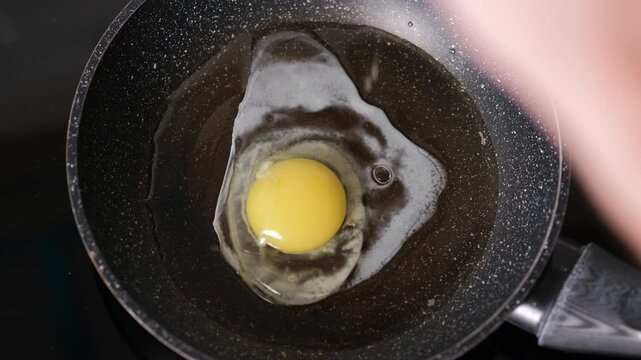 Hands of a man cracking fresh eggs into a hot frying pan from top view, morning cooking scene, home breakfast preparation concept