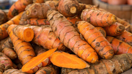 Close-up of fresh organic turmeric roots, some cut open to reveal their vibrant orange color and earthy texture, ready for culinary and medicinal uses