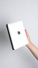 A hand holds a white, rectangular device with black edges, against a white background in vertical shot