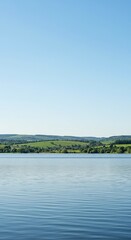 A vast expanse of tranquil reservoir water under a bright summer sky, reflecting verdant green hills and a clear distant horizon ,idyllic ,landscape ,sun