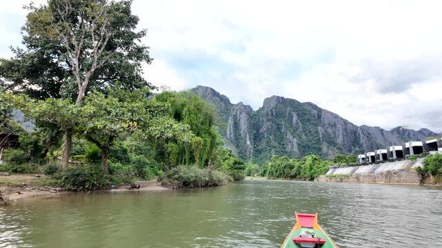 Peaceful Laos landscape with a colorful longtail boat on the Nam Song river near lush mountains.