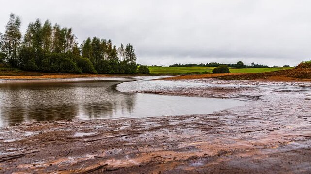 Murky river with muddy riverbank drains as the tide goes out, under cloudy sky