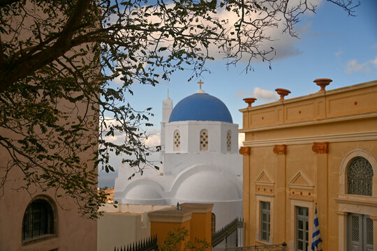 The national flag of Greece flying in front of a blue church steeple. - Powered by Adobe