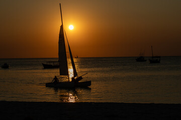 Sailboat and small dinghy in silhouette against a dramatic African sunset over the ocean in...