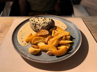 close up of steak with creamy peppercorn sauce and roasted potatoes on a plate at a restaurant outdoors at night 