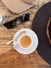 directly above shot of espresso macchiato coffee on table with sunglasses and hat at a cafe
