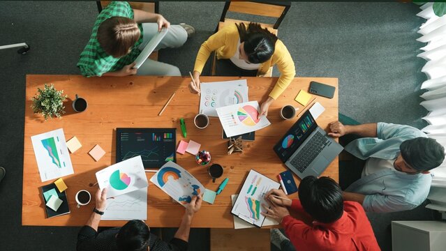 Top down view of investor brainstorming while looking at financial statistic document. Group of diverse people sharing marketing idea or planning marketing campaign with skilled leader. Convocation. - Powered by Adobe