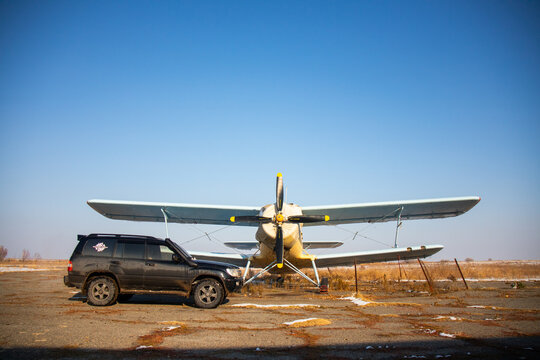 Naryn, Kyrgyzstan - December 13, 2025: A black Toyota Land Cruiser 100 4x4 parked on an abandoned runway with an Antonov An-2 biplane propeller aircraft in the background