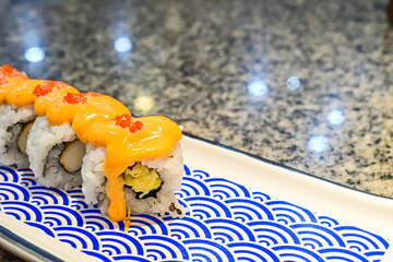 Delicious sushi rolls with spicy sauce and fresh ingredients at a local Asian restaurant. Close up view. mentai. long plate. japanese, japan. blue, white. seaweed. copy space, empty, free, negative.