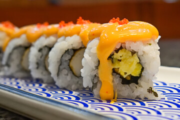 Delicious sushi rolls with spicy sauce and fresh ingredients at a local Asian restaurant. Close up view. mentai. long plate. japanese, japan. blue, white. seaweed.