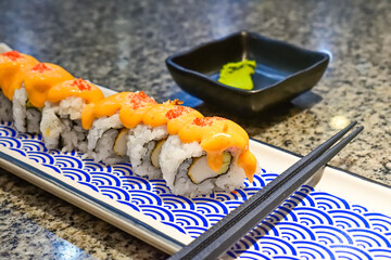Delicious sushi rolls with spicy sauce and fresh ingredients at a local Asian restaurant. Close up view. mentai. long plate. japanese, japan. blue, white. black chopsticks. wasabi. copy space. seaweed