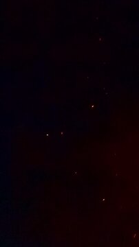 Small red embers rise and move in dark smoky night atmosphere creating floating glowing particles from distant fire with dynamic warm light and cinematic texture