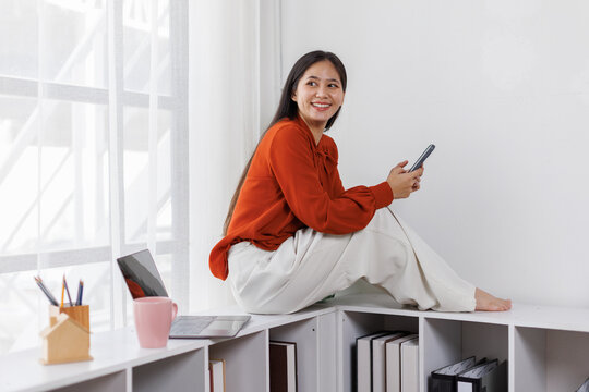 relaxed asian woman drink coffee and use mobile phone at office
 - Powered by Adobe