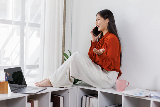 relaxed asian woman drink coffee and use mobile phone at office
