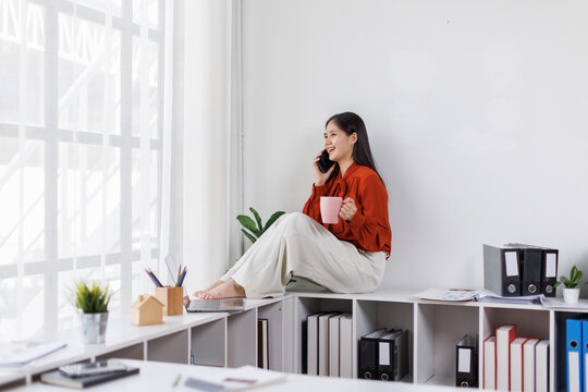 relaxed asian woman drink coffee and use mobile phone at office
