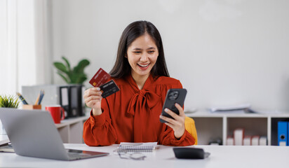 One young beautiful caucasian business asian woman is buying online on her mobile phone using credit card from her home