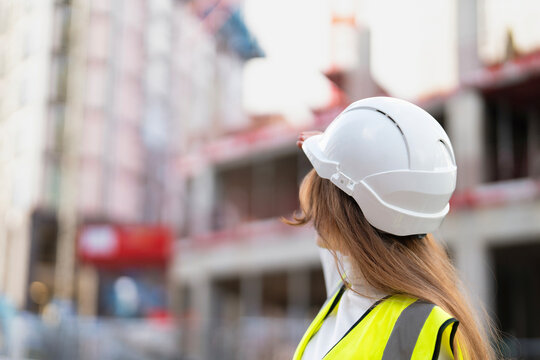 Woman builder in white helmet observes building progress at construction site