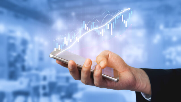 A hand holds a smartphone displaying a financial growth graph featuring an upward arrow. This image represents progress, investment, and modern technology in business. Impute