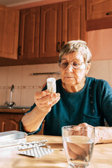 An elderly woman carefully reads the instructions on a bottle of medication. Age-related medication confusion, problems with home care, and medication hesitancy