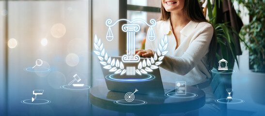Smiling woman at a table using a laptop with legal icons in a bright office space