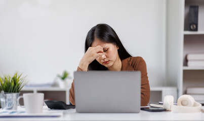 Sad and frustrated asian woman feeling tired and worried about a problem sitting at desk with laptop, stressed and in pain female having problems reading bad news online, email notification about debt