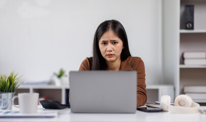 Sad and frustrated asian woman feeling tired and worried about a problem sitting at desk with laptop, stressed and in pain female having problems reading bad news online, email notification about debt