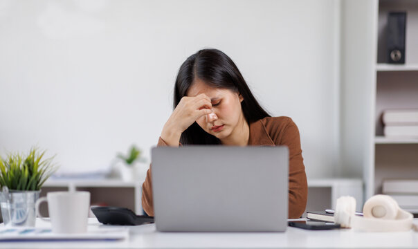 Sad and frustrated asian woman feeling tired and worried about a problem sitting at desk with laptop, stressed and in pain female having problems reading bad news online, email notification about debt - Powered by Adobe