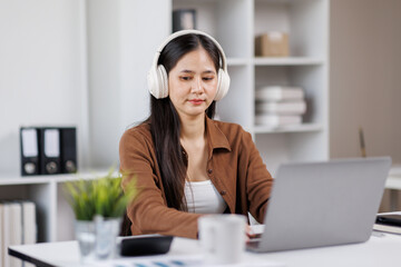 Smiling woman takes notes at her office, wearing headphones listening music at work using laptop remote work. Online education concept
