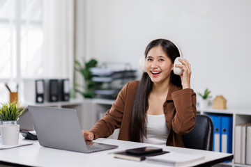 Smiling woman takes notes at her office, wearing headphones listening music at work using laptop remote work. Online education concept
