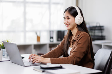 Smiling woman takes notes at her office, wearing headphones listening music at work using laptop remote work. Online education concept
