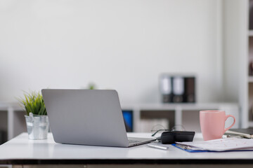 Laptop Computer, notebook, and eyeglasses sitting on a desk in a large open plan office space after working hours	