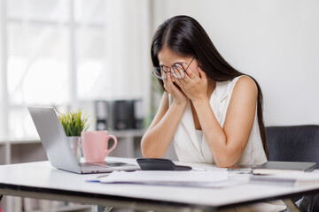 Portrait of tired sad business Asian woman work with documents tax laptop computer in office. Sad, unhappy, Worried, Depression, or employee life stress concept
