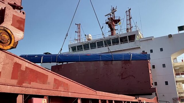 Unloading steel products from the cargo hold of a cargo ship using a port crane and lifting slings. Safe cargo handling operations in a commercial seaport and maritime logistics.