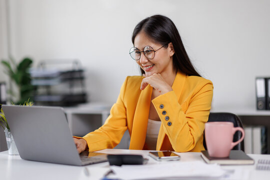 Asian woman smiles while working on her laptop at a bright, modern office desk. happy businesswoman with his work in the office.