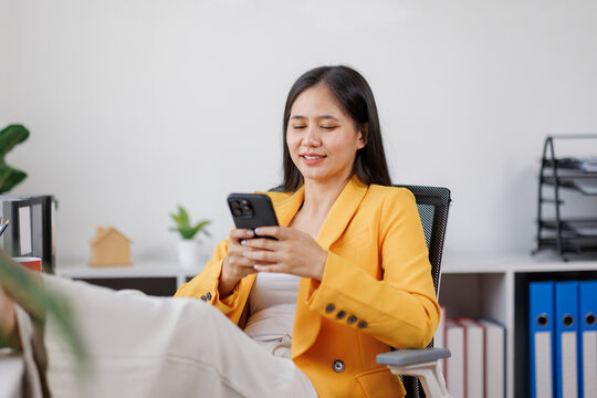 Happy asian woman, phone and smile for social media, communication or networking at work. Female freelancer smiling on mobile smartphone app for chatting, texting or browsing on internet or research

