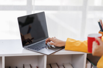 Young asian businesswoman working with modern laptop and cup of hot coffee at table in the office.
