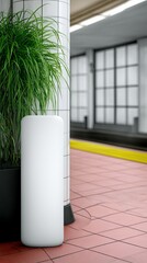 A blank white display stand and a large potted plant are positioned on a subway platform, with a yellow safety line visible.