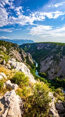 Aerial view of a winding river flowing through a rocky canyon under a bright blue sky with fluffy clouds