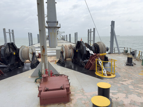Forward mooring station of cargo ship showing windlass, mooring winches, ropes, and anchor chain. 1