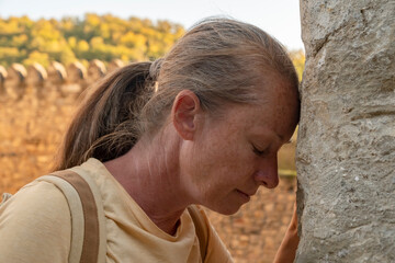 Woman resting her forehead against a stone wall while enjoying sunset at a historic location