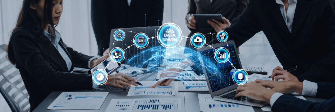 A group of business professionals engage in a strategic meeting in a modern office, utilizing advanced data-driven tools for informed decision-making and collaboration. Trope - Powered by Adobe